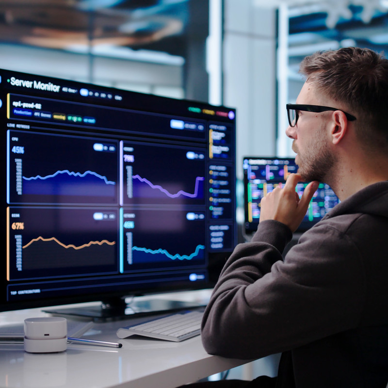 Engineer monitoring SCADA dashboards and system data across multiple computer screens.