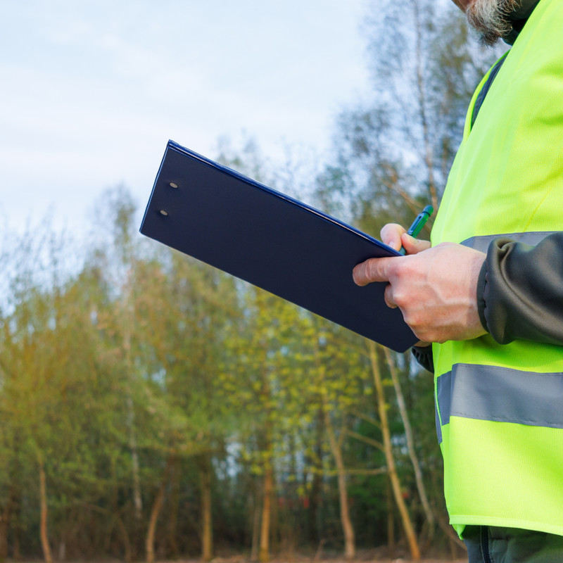 Engineer in a high-visibility vest recording information during a field inspection.